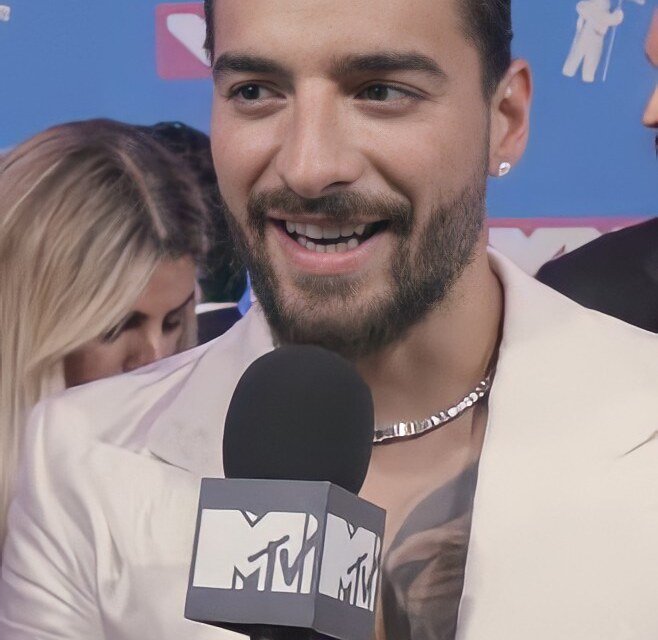 Maluma, smiling, in a white suit, holding an MTV microphone