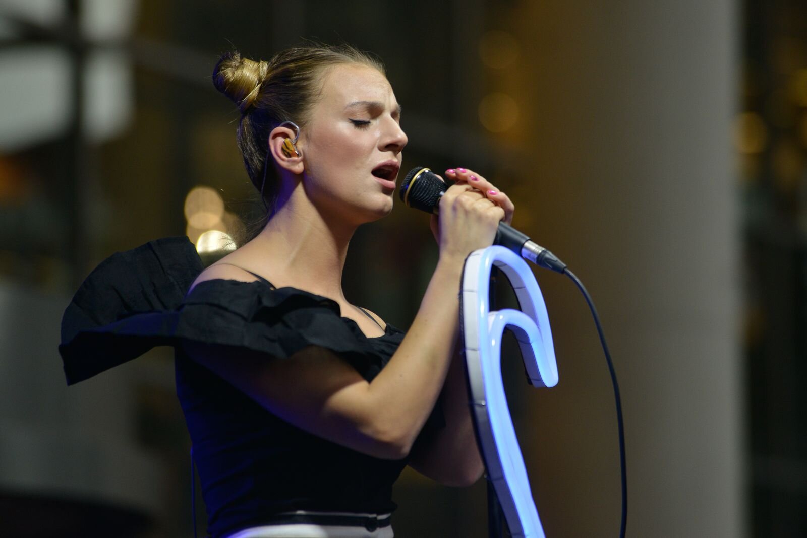 Sarsa singing on stage with her eyes closed, holding the microphone in both hands, her hair in a bun, in a black top
