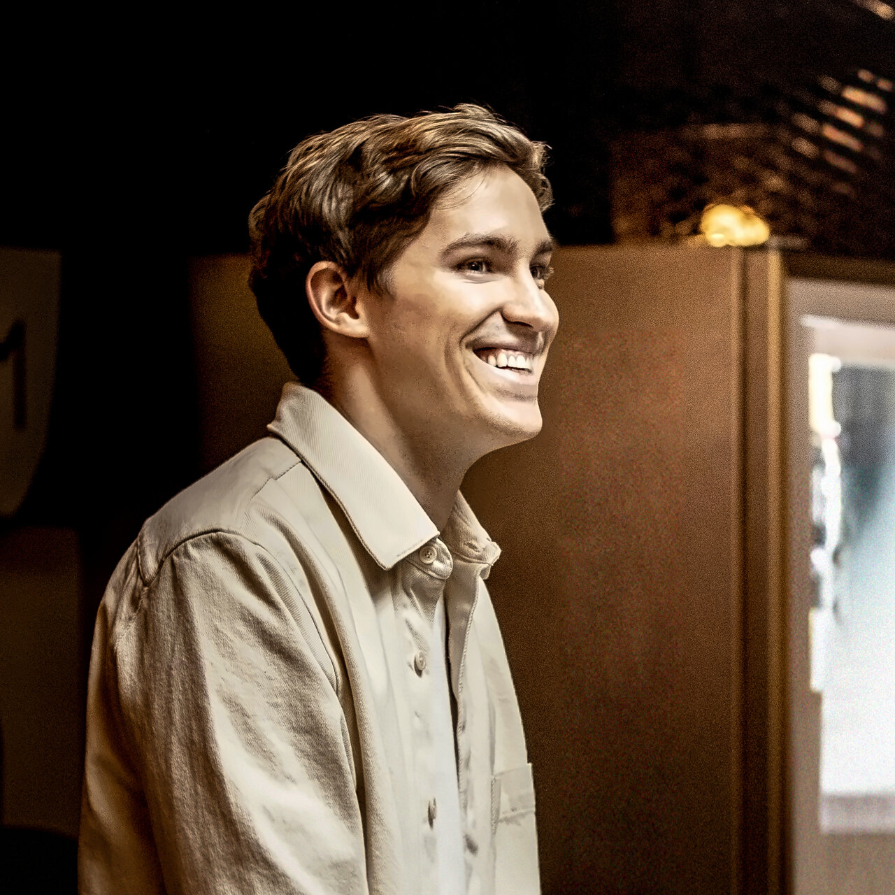 Mati Staniszewski, smiling, in a light shirt, in warm light against a dark background